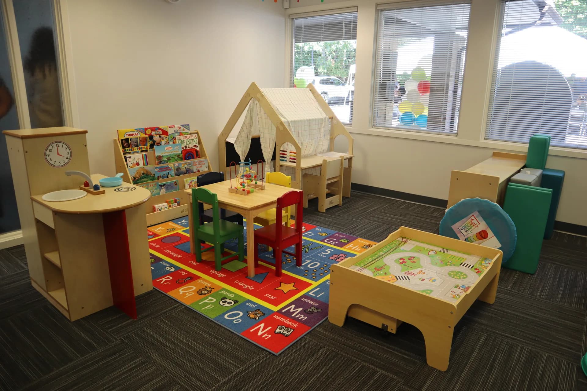 Inside our Middletown clinic - a warm, light-filled children's playroom with a wooden play house, alphabet rug, child-sized table, and bookshelves.
